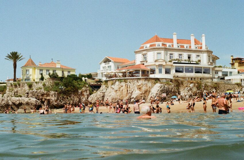 Crowded beach scene at Cascais, Portugal, featuring sunbathers by the oceanfront resort.