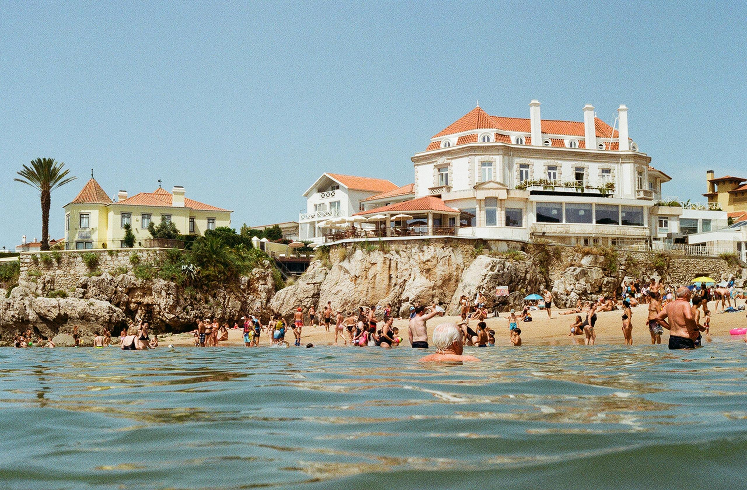 Crowded beach scene at Cascais, Portugal, featuring sunbathers by the oceanfront resort.