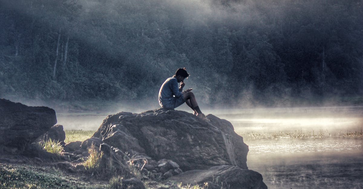 pexels photo 694458 694458 A lone figure reflects on a rock by a misty lake in Rancabali amidst tranquil surroundings.